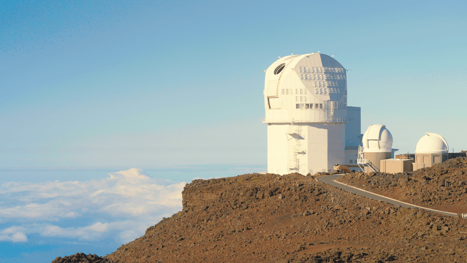 holistic health A white domed structure on top of a dirt mountain. It appears to be above the clouds in the distant sky. Inouye Solar Telescope