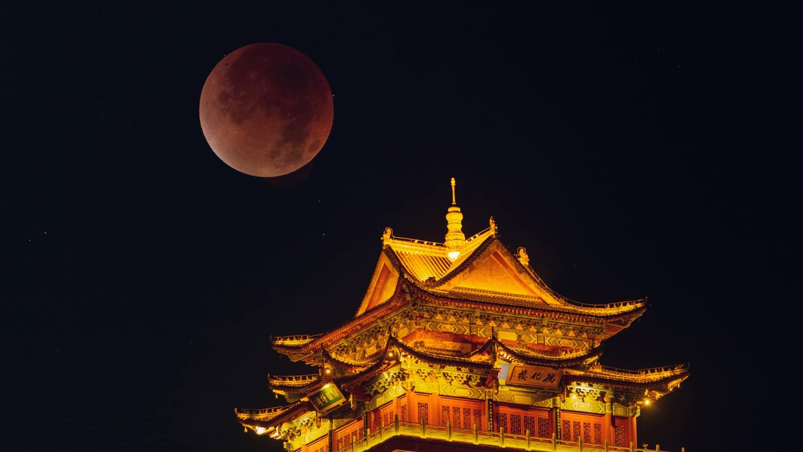 nature A red moon is visible in a dark sky above a yellow-lit building with a pointed roof.