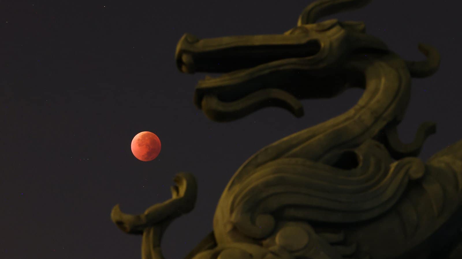nature A blood red moon is positioned against the dark sky to appear as if it is held in the claw of a stone dragon statue in the foreground.
