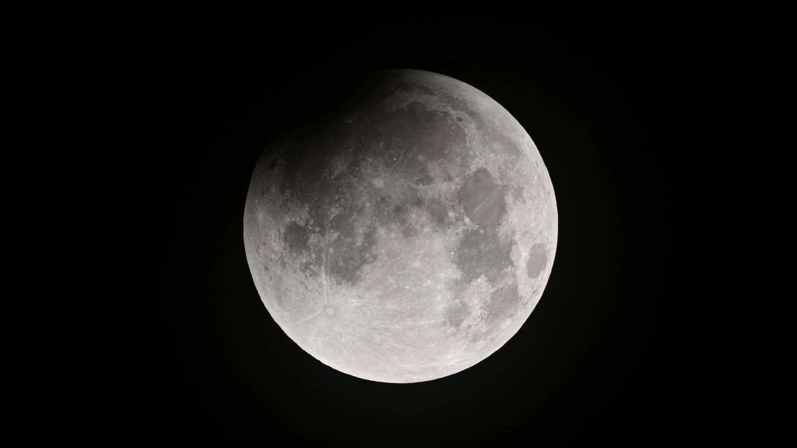 nature A full moon is pictured against a dark sky. Dark features called lunar maria are visible marking its surface and an impenetrable shadow has fallen over the upper right edge of the lunar disk.