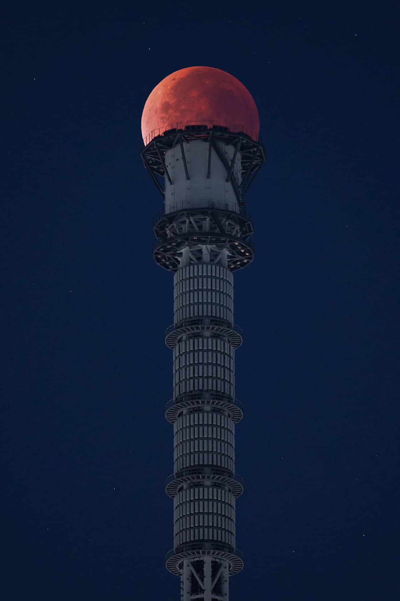 nature A red full moon is positioned atop a tower in Japan against a dark blue night sky.